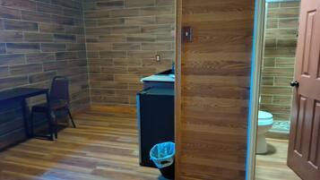 A room with a wooden floor, a desk with a chair, and a wooden wall.