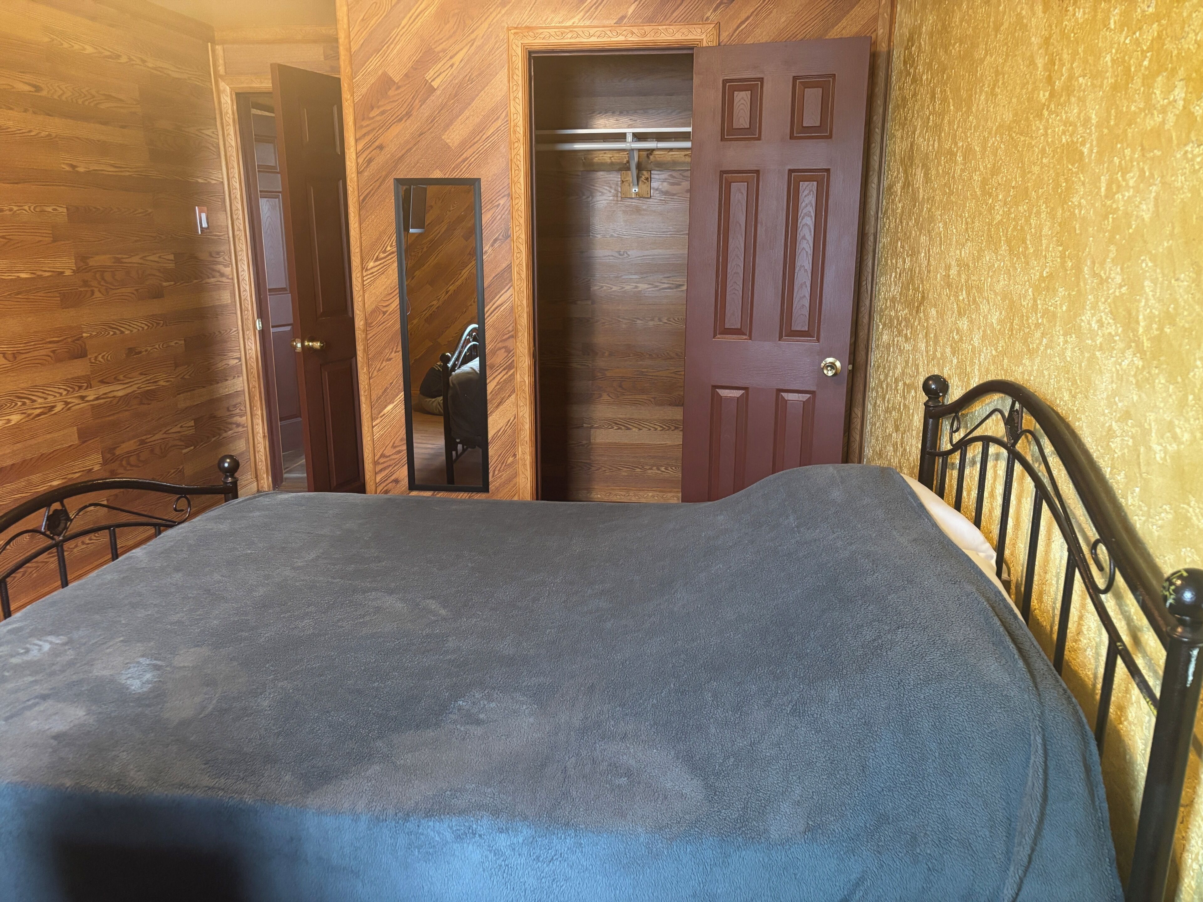 Un dormitorio con cama, paredes de madera, una puerta y un espejo.