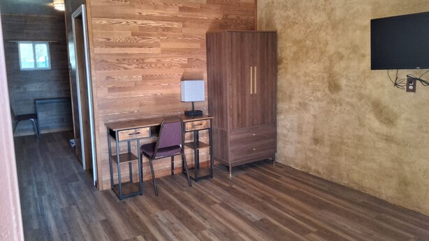 A room with a wooden desk, a chair, a wardrobe, and a television mounted on the wall. - The Mint Motel (Arlington)