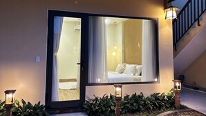 A hotel room with a large sliding glass door, a bed with white bedding, and a staircase with a thatched roof. - Lá Home (Hue)