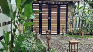 A rustic thatched-roof hut surrounded by lush greenery and a stone wall. - Lá Home (Hue)