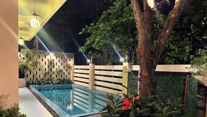 A swimming pool with a tiled deck, surrounded by potted plants and a wooden fence. - Lá Home (Hue)