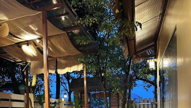 An outdoor area with a stone pathway, wooden pergola, and seating under a canopy. - Lá Home (Hue)