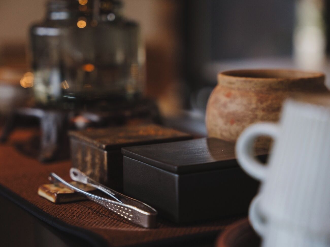 A table with a coffee maker, a teapot, a box, and a pair of tongs.