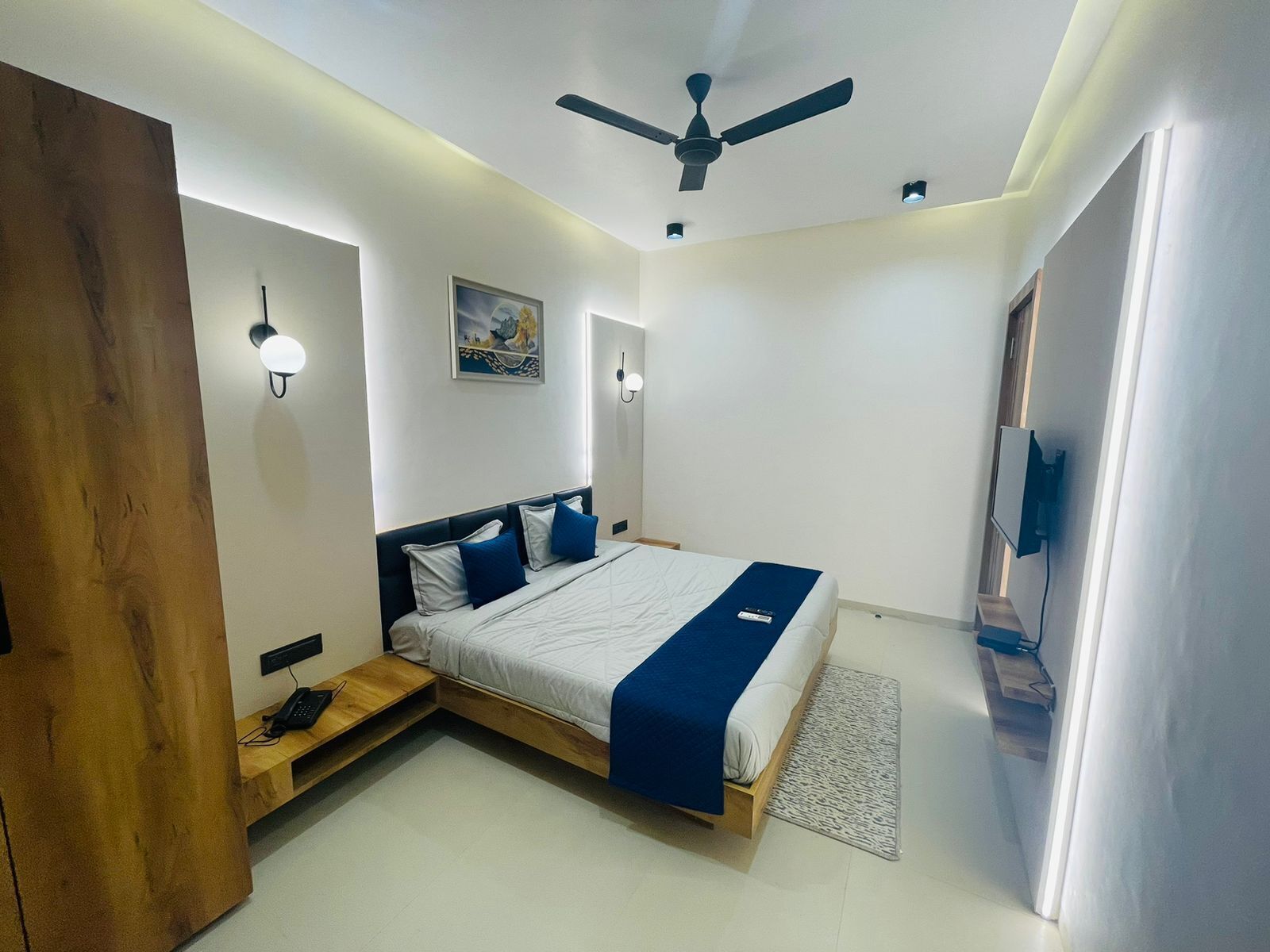 A modern bedroom with a bed, bedside tables, a ceiling fan, and a mounted TV.