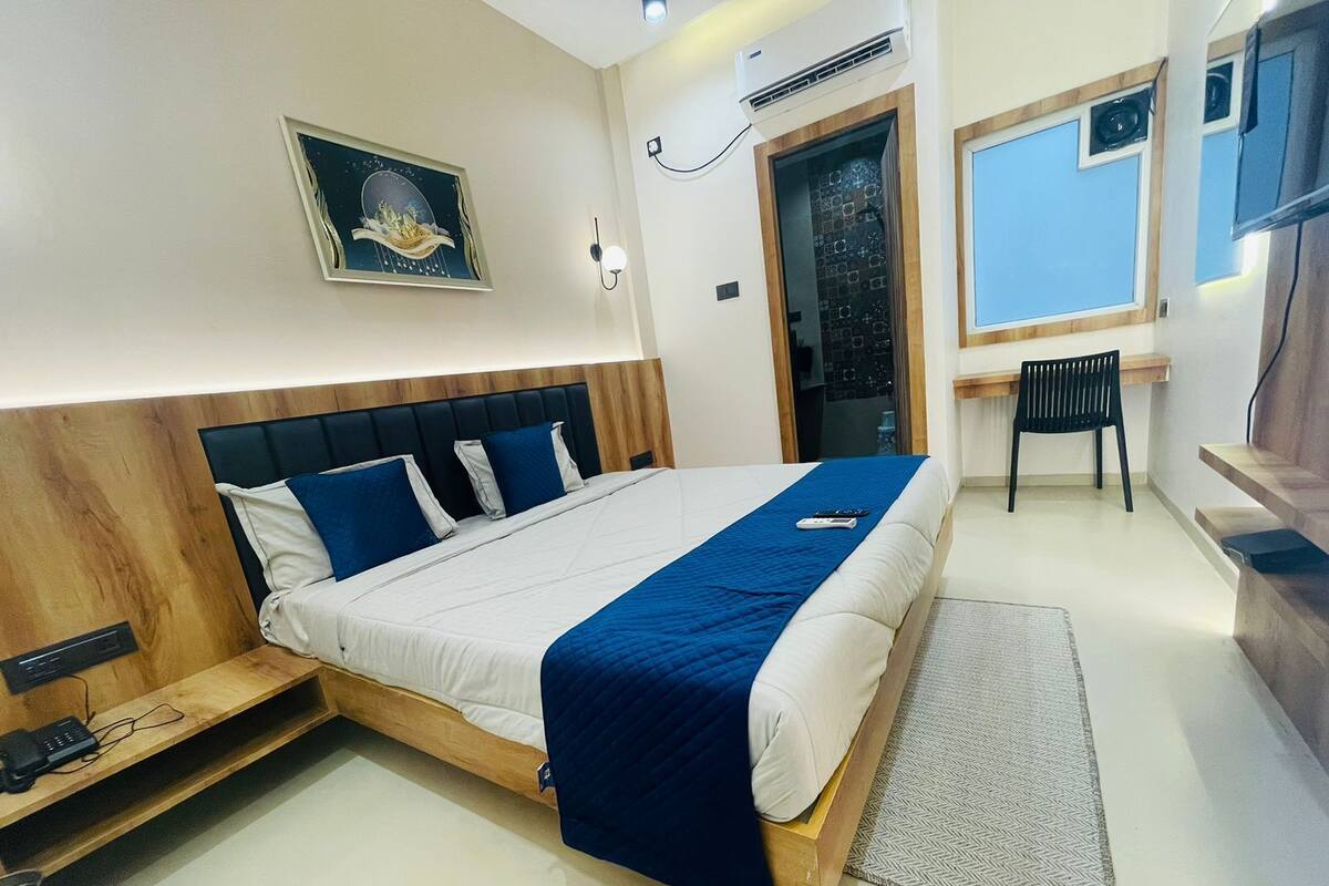 Ett modernt hotellrum med en stor säng, ett skrivbord med en stol, en TV och en dörr som leder till ett badrum.
