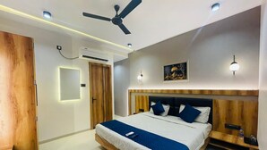 A modern bedroom with a wooden bed frame, a ceiling fan, recessed lighting, and a nightstand with a water bottle. - Hotel The Golden Tree (Damoh)