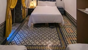 A hotel room with a bed, a nightstand, a mirror, and a patterned floor. - dar fes flower (Fès)