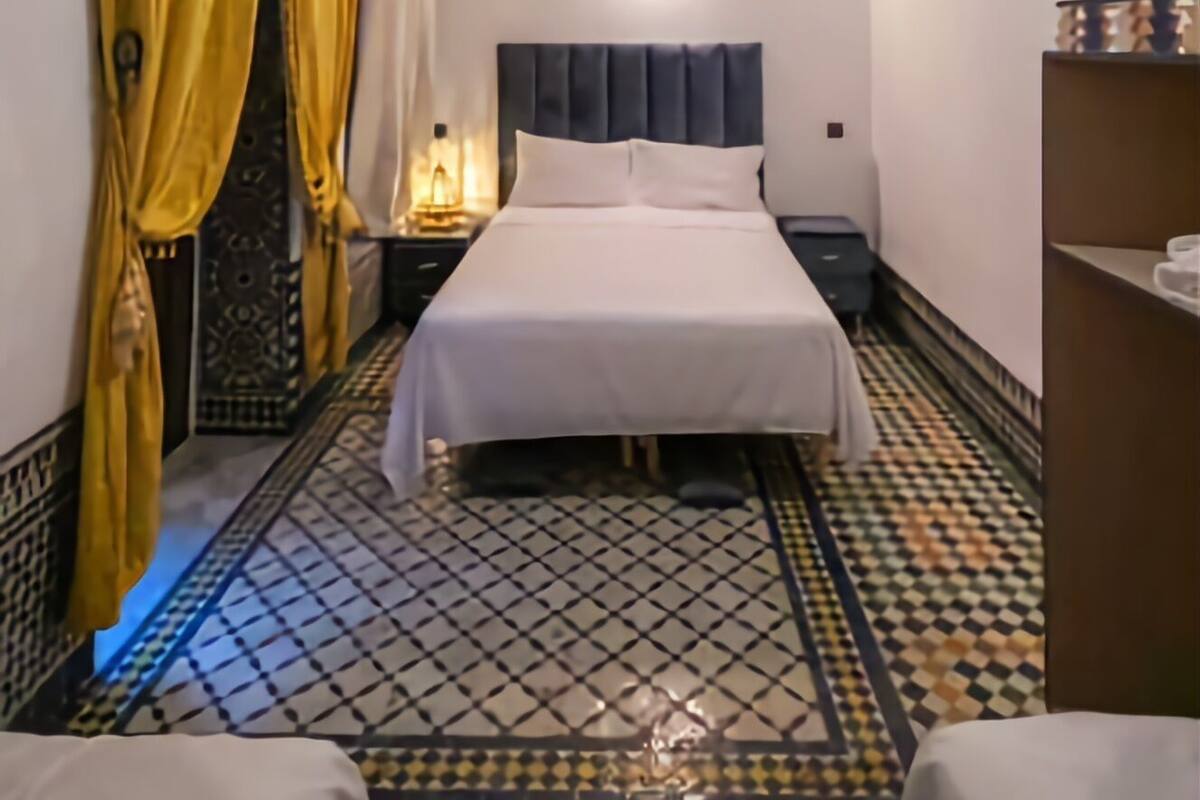 Une chambre d’hôtel avec un lit, une table de chevet, un miroir et un sol à motifs.