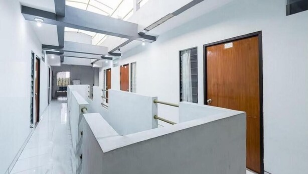 A modern hotel corridor with a skylight, white walls, and wooden doors. - Hotel Cemara Gading (Dramaga)