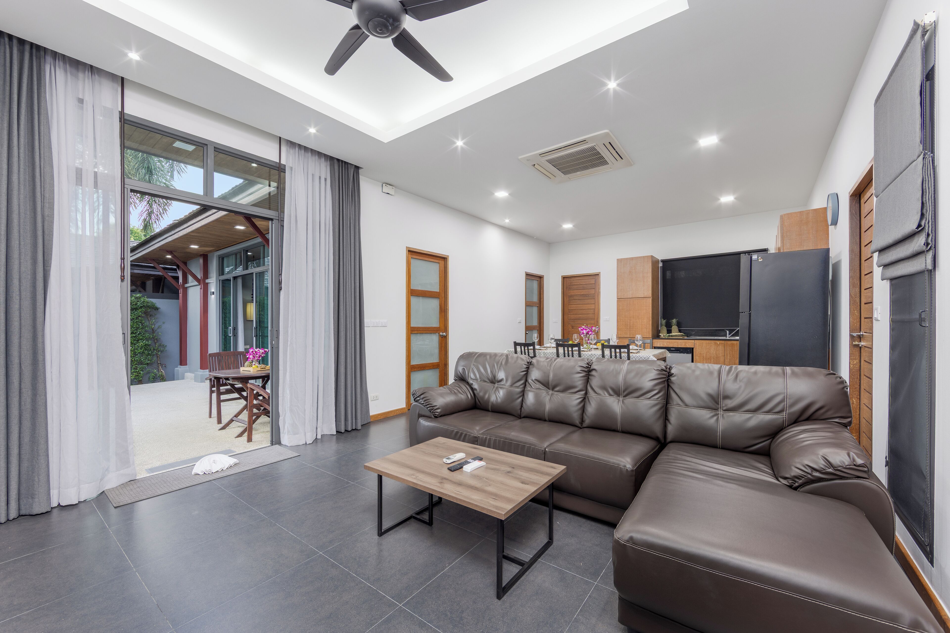 Ein modernes Wohnzimmer mit Ledersofa, Couchtisch aus Holz und Deckenventilator.