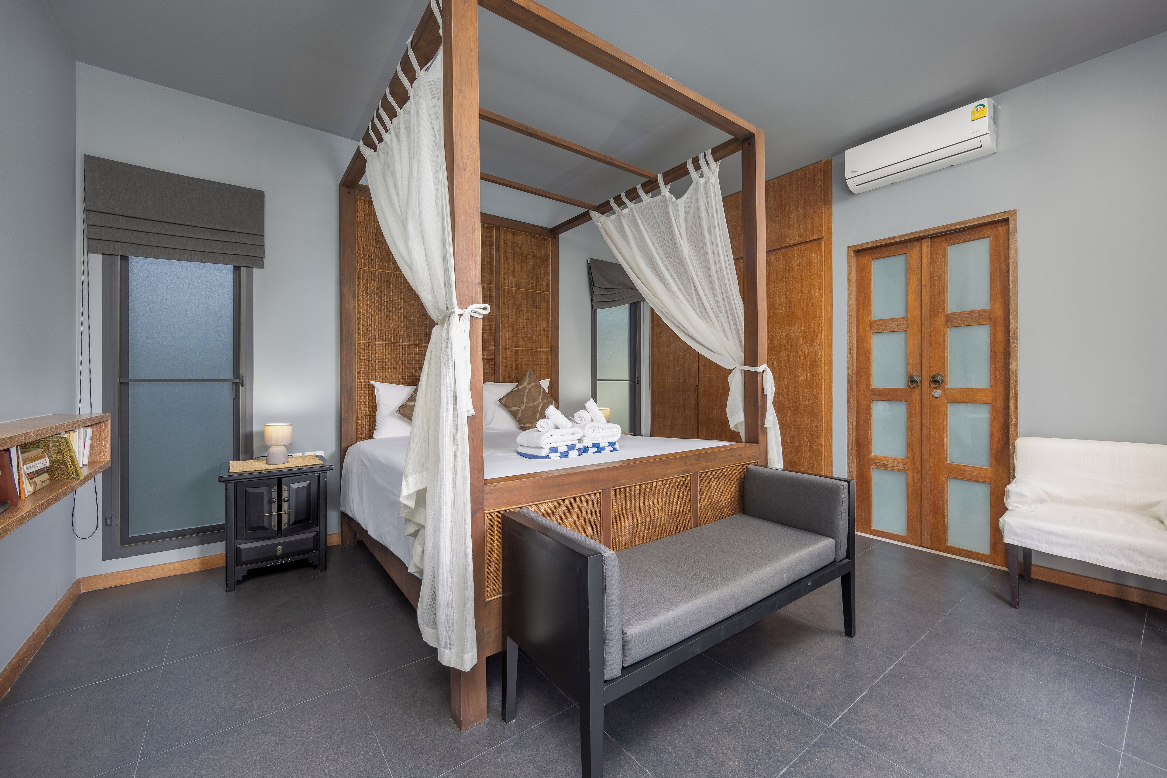 A four-poster canopy bed with a bench, bedside table, and a nightstand with a lamp.