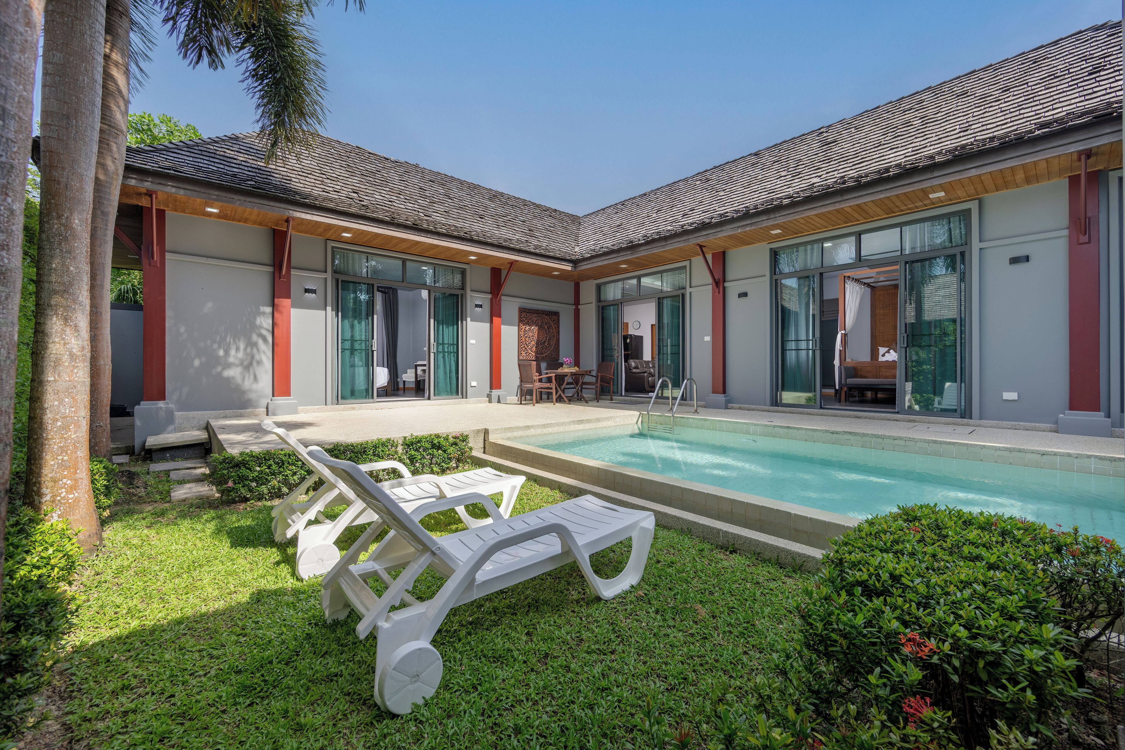 A modern house with a swimming pool, two lounge chairs, and a patio area.