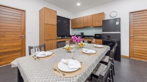 A dining area with a table set for four, wooden cabinets, a clock on the wall, and a refrigerator. - Villa Kiana Private Pool 10 min Nai Harn (Rawai)