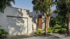 A modern house with a garage, a concrete driveway, and a well-maintained garden with various plants and a tree. - Villa Kiana Private Pool 10 min Nai Harn (Rawai)