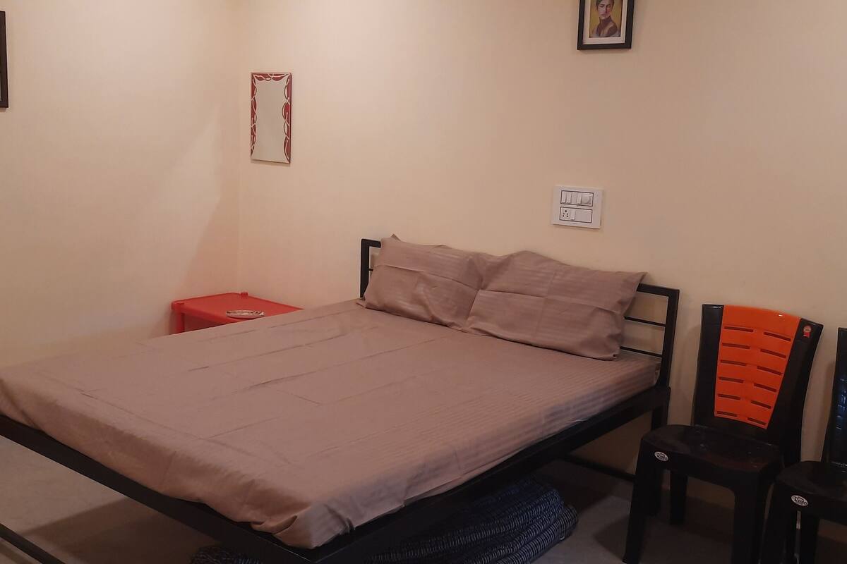 A single bed with a headboard, a red nightstand, and two chairs with yellow and black backs.