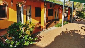Un bâtiment jaune avec une entrée abritée, des plantes en pot et un sol sablonneux.