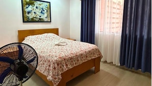 A bedroom with a wooden bed, a wall-mounted fan, and a window with blue curtains. - Casa Terracota: Lovely 3-bedroom house in Atenas Perfect for Relaxing Getaways (Atenas)