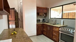 A kitchen with wooden cabinets, a granite countertop, a built-in oven, and a window with bamboo blinds. - Casa Terracota: Lovely 3-bedroom house in Atenas Perfect for Relaxing Getaways (Atenas)