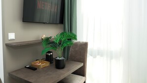 A modern living room with a flat-screen TV mounted on the wall, a potted plant, a remote control, and a small wooden box on a table. - Living Inn (Rheda-Wiedenbrück)