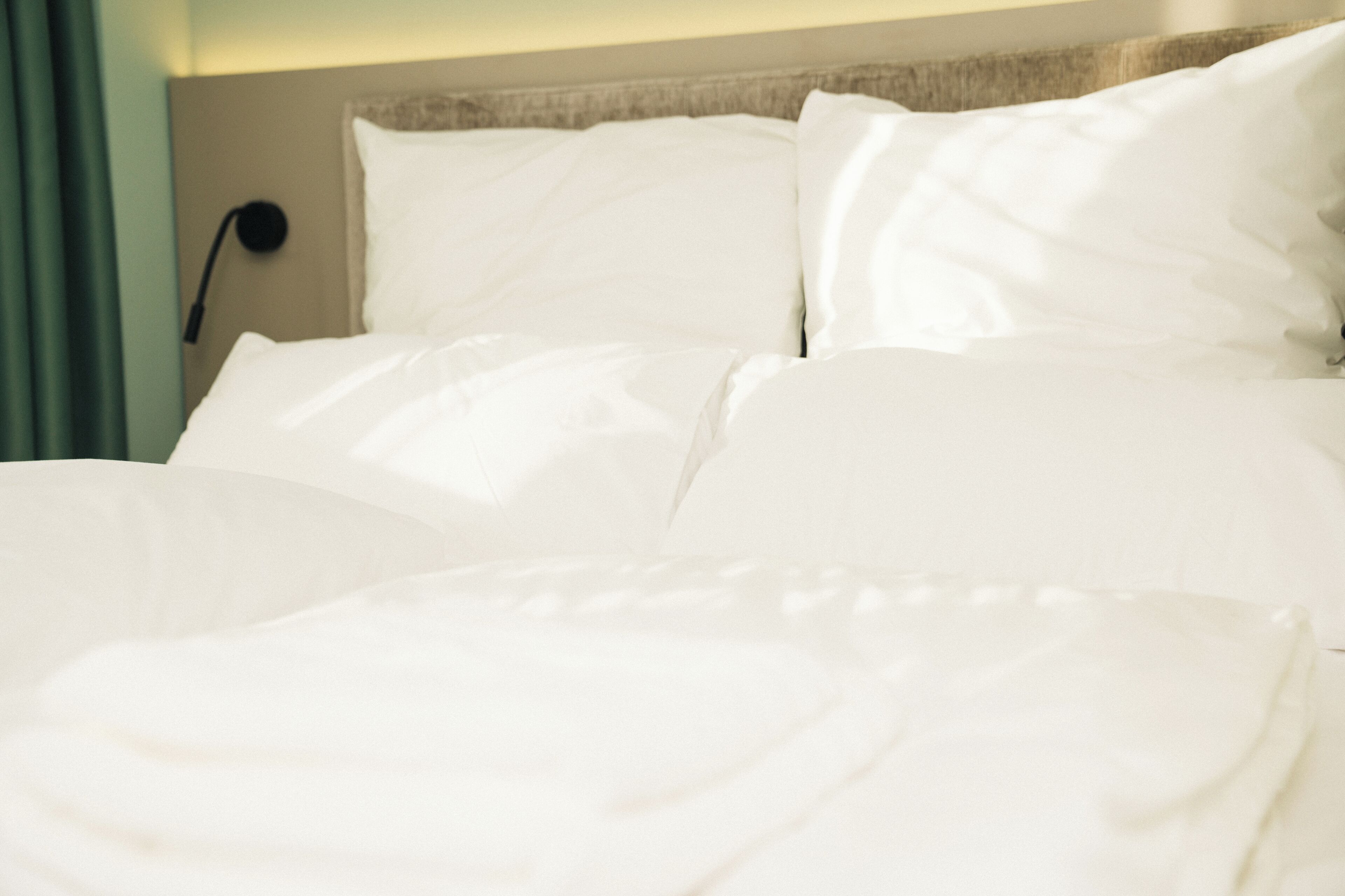 Cama bem arrumada com roupa de cama branca e cabeceira.