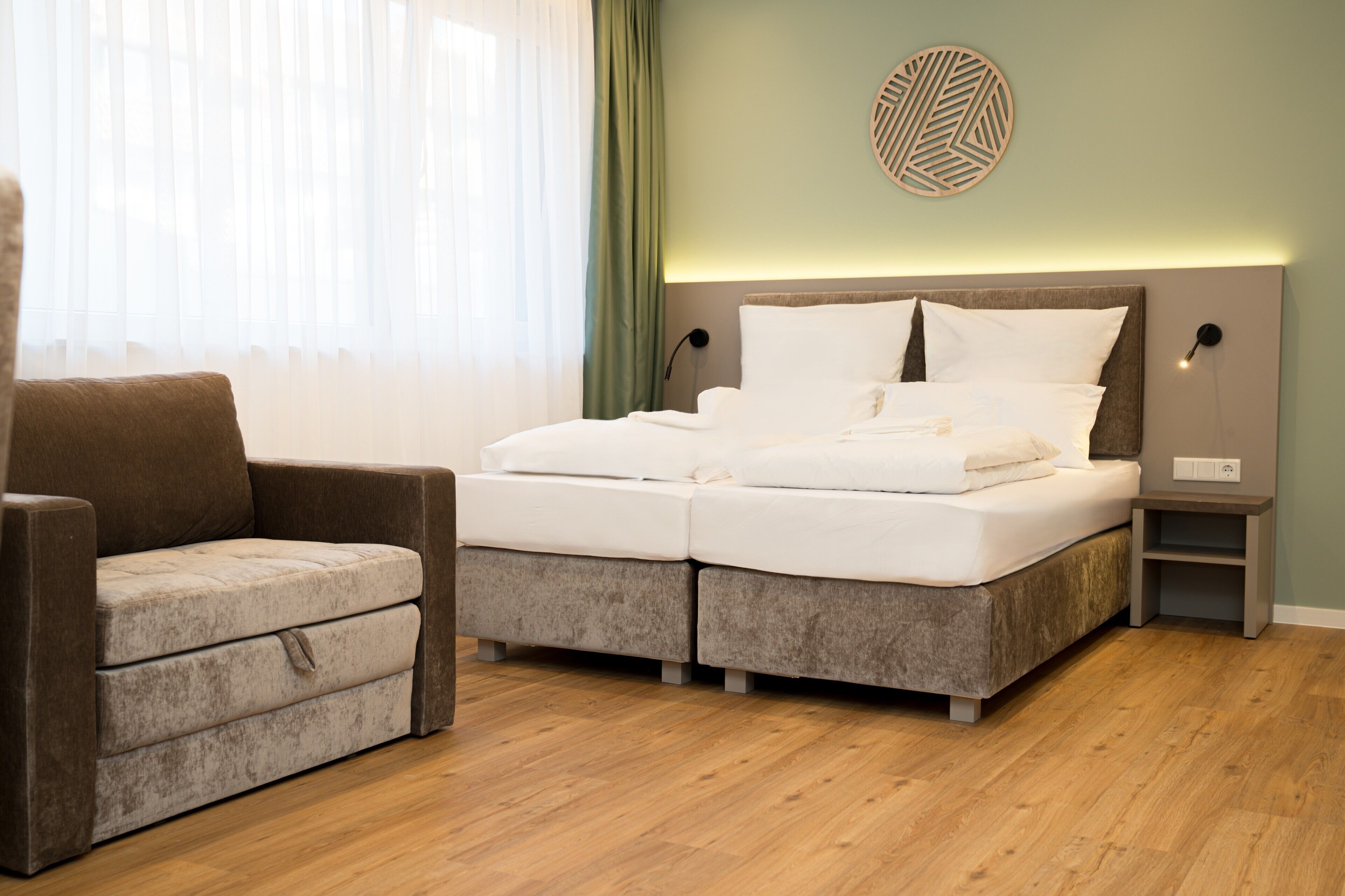 Un dormitorio con cama, una silla, una mesita de noche y una lámpara fijada en la pared.