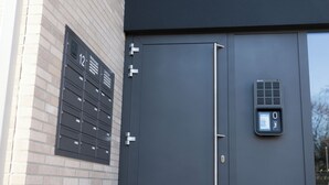 A modern building facade with a dark grey door, a mailbox with a number '12' sign, and a security keypad. - Living Inn (Rheda-Wiedenbrück)