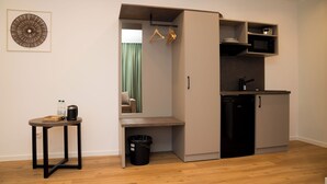 A compact kitchenette with a microwave, sink, and cabinets, a small table with a tray and bottles, and a hanging coat rack. - Living Inn (Rheda-Wiedenbrück)