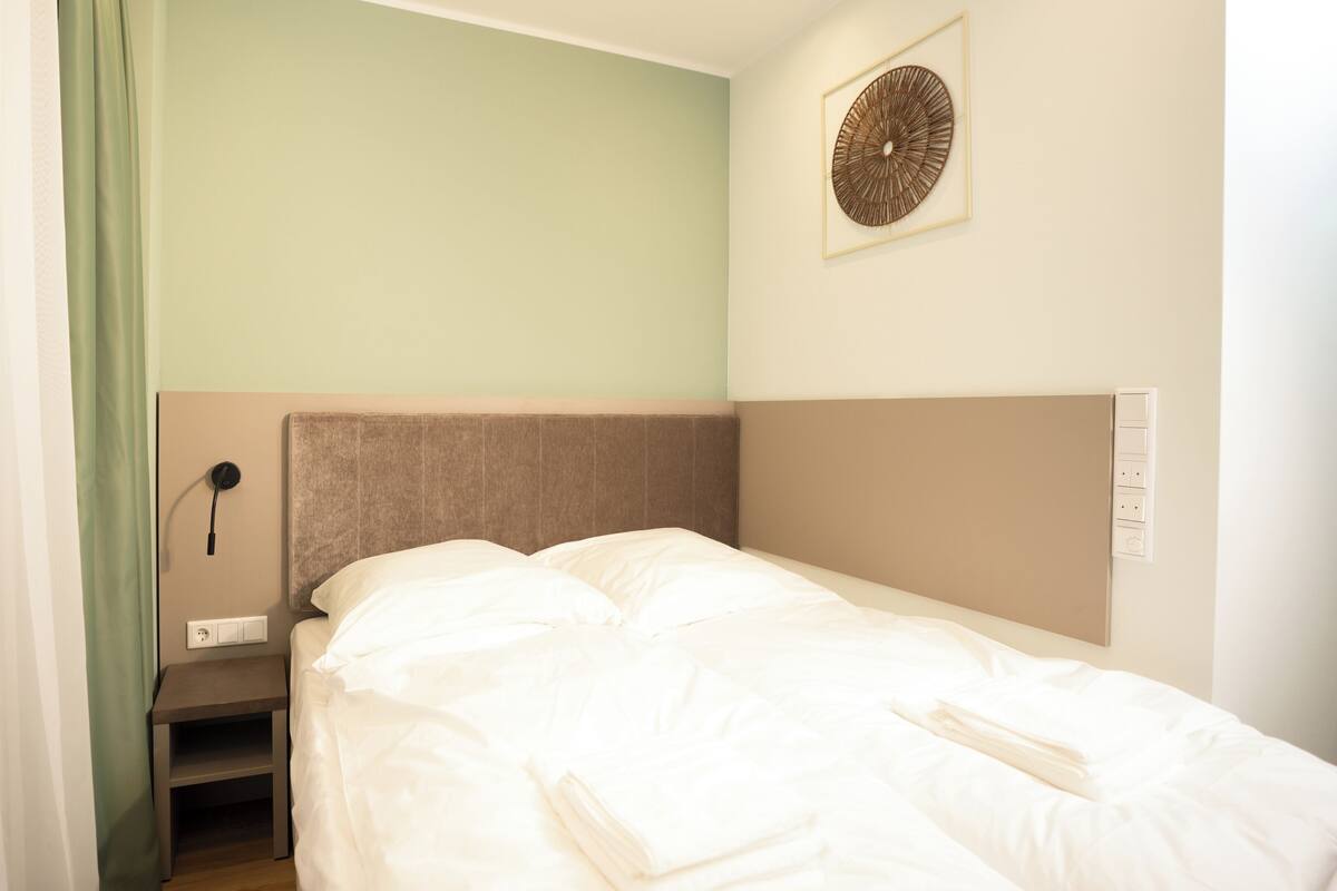 Un lit bien fait, avec du linge de lit blanc, une tête de lit et un luminaire fixé au mur.