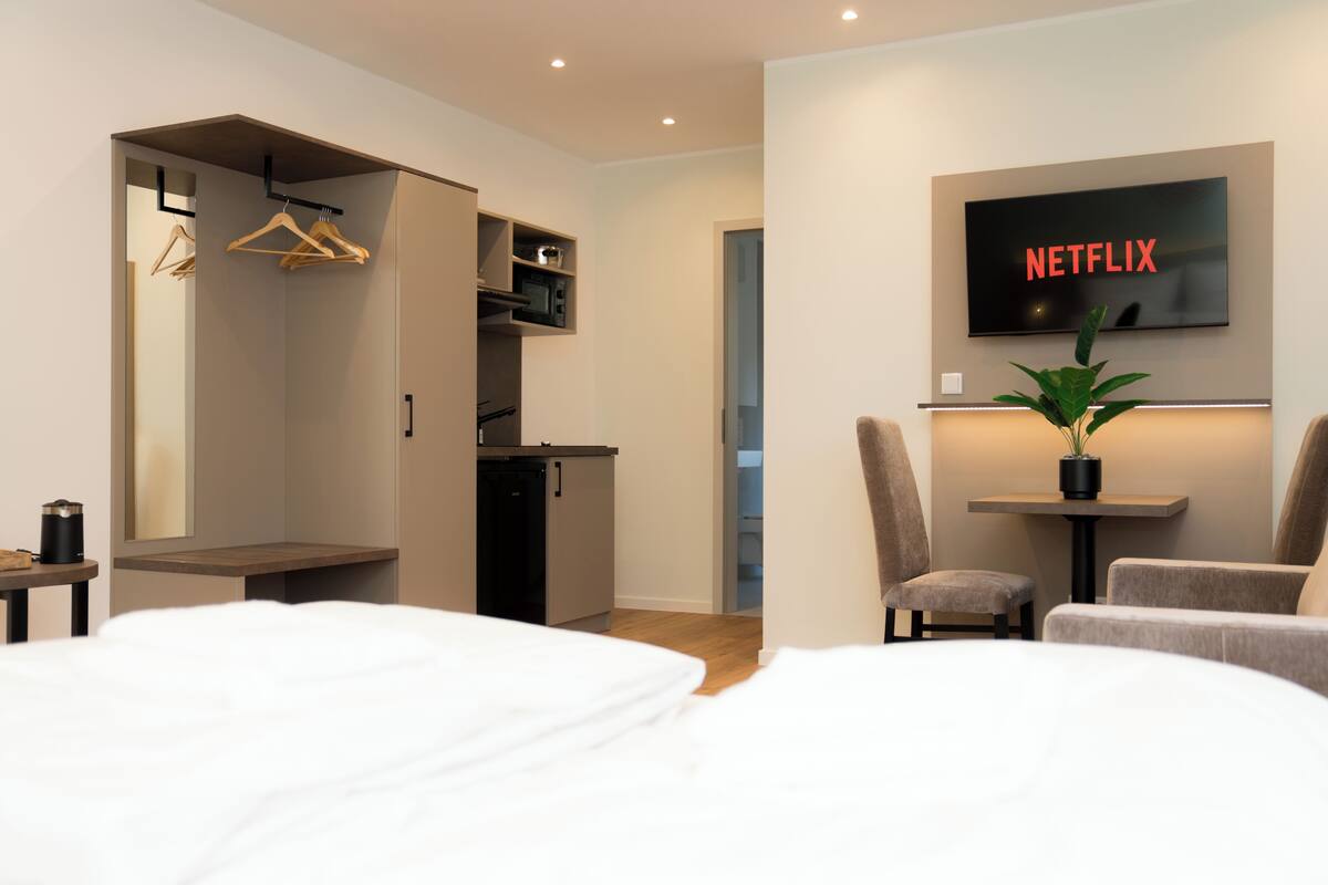 Une chambre d’hôtel moderne équipée d’un lit, d’un bureau, d’une chaise, d’un téléviseur fixé au mur et d’une armoire.