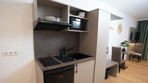 A compact kitchen with a dishwasher, microwave, and a small sink. There is a dining area with a chair and a table. - Living Inn (Rheda-Wiedenbrück)