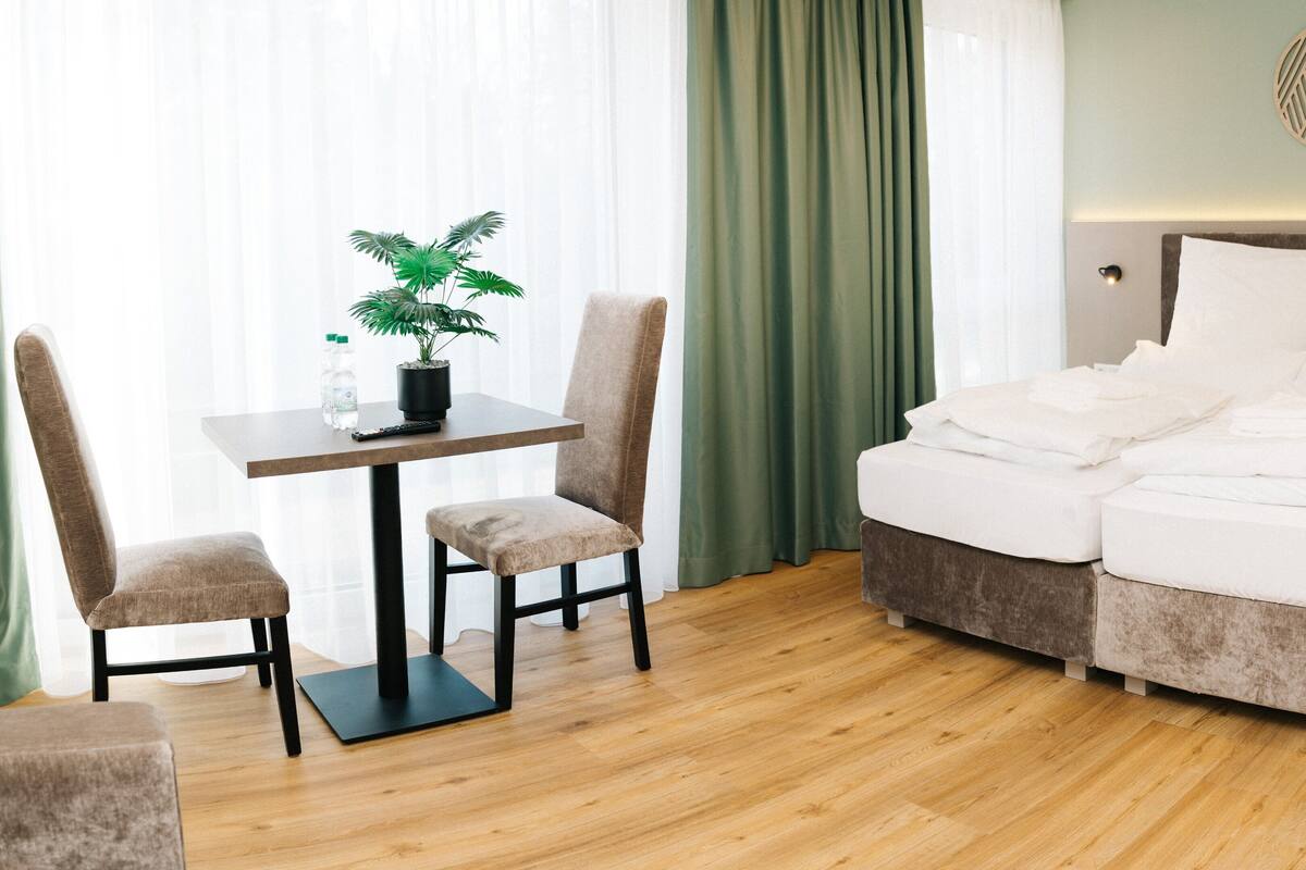 Une chambre d’hôtel avec un lit, une table et des chaises, une plante en pot et un luminaire fixé au mur.