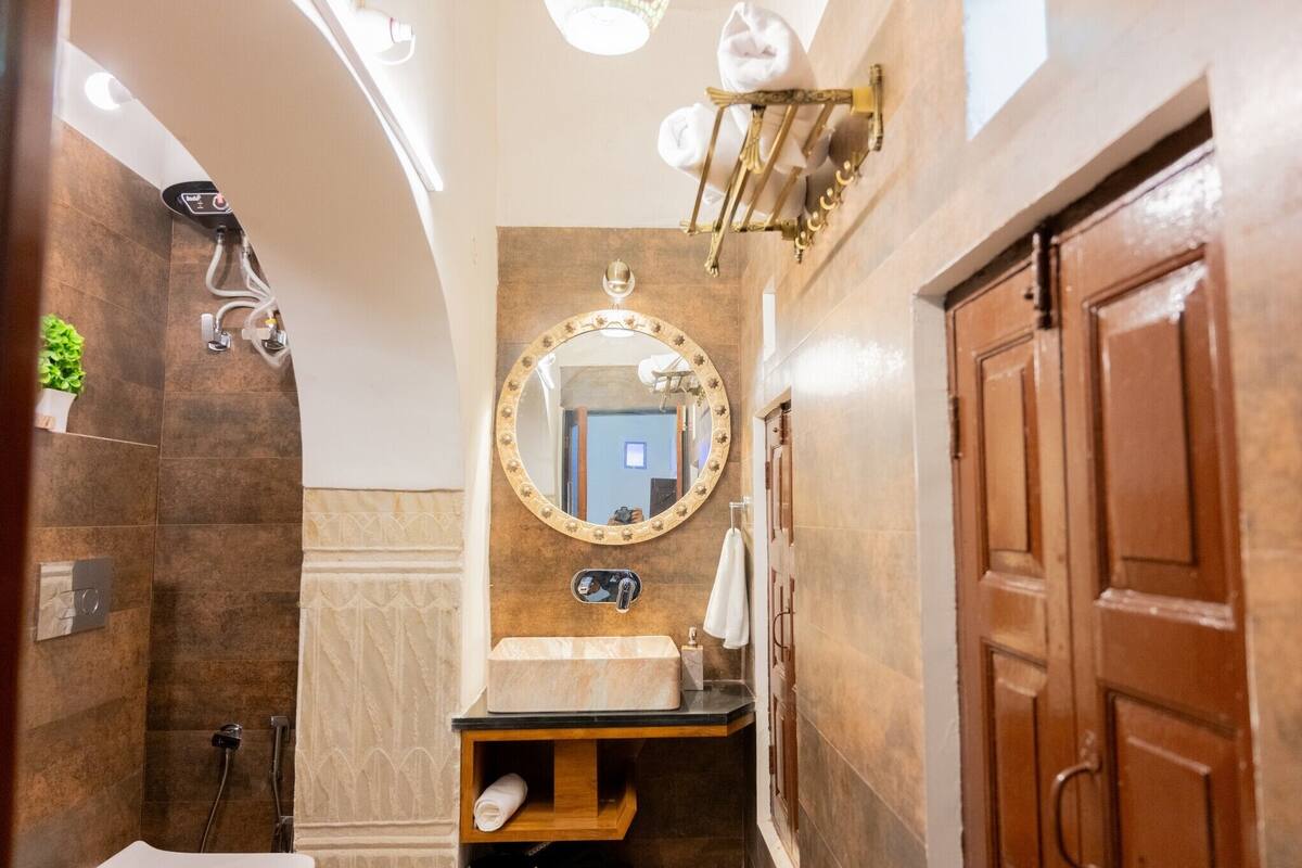 Un baño con un lavamanos de mármol, un espejo redondo con marco dorado, un perchero y una puerta de madera.