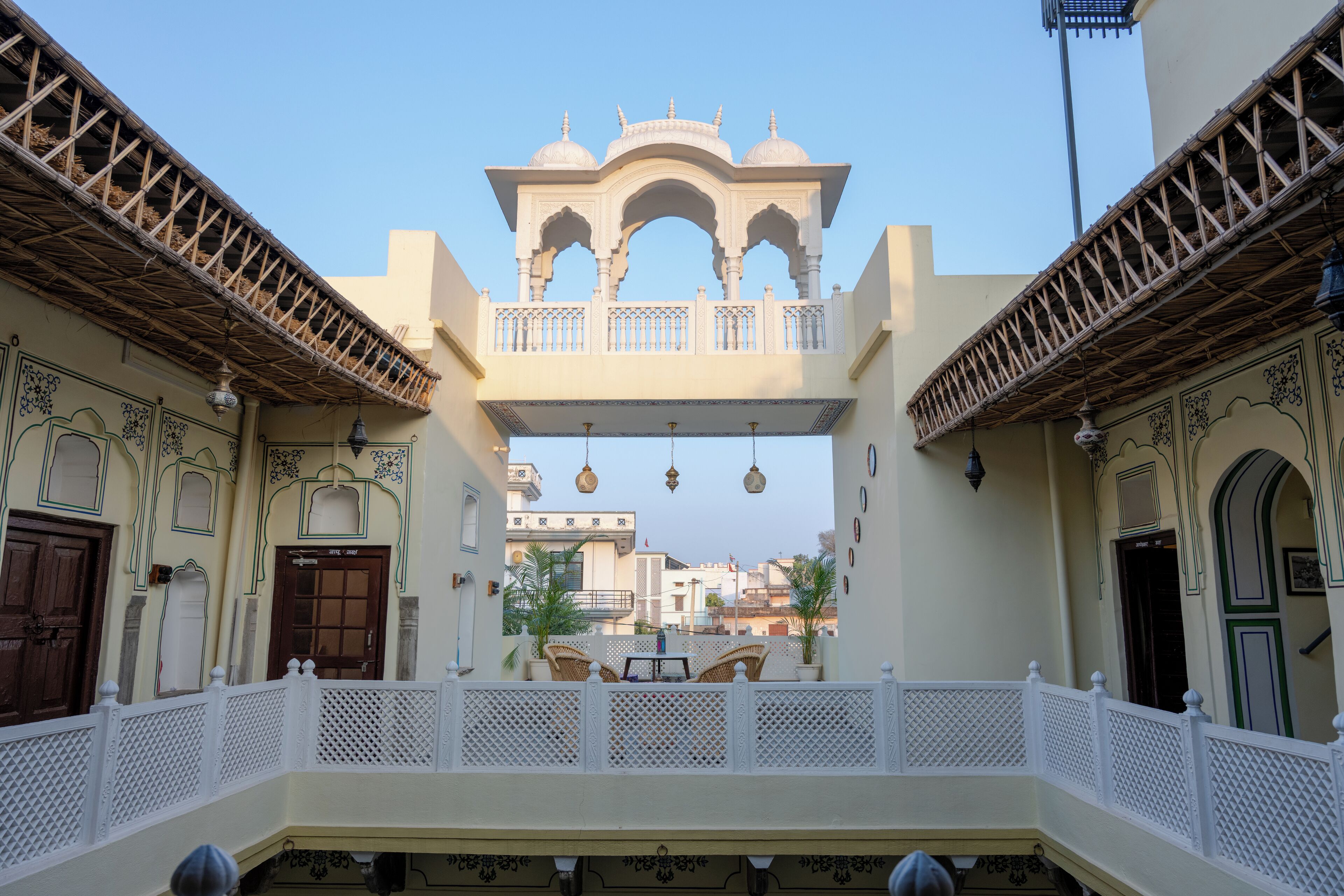 A traditional building with a central archway, white lattice railings, and a balcony with wicker furniture.