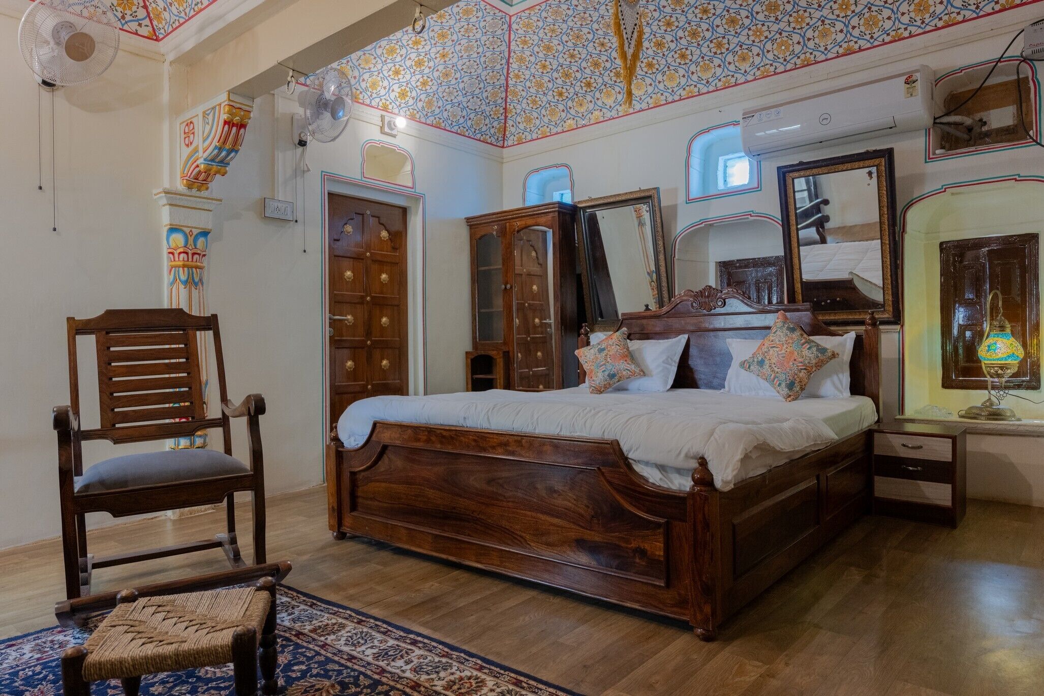 Un dormitorio con cama de madera, una silla, una mesita y un espejo.