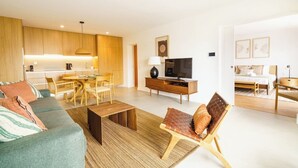 A modern living room with a sofa, coffee table, and a TV. There's a dining area with a table and chairs. The room has wooden cabinets and a kitchen in the background. - Carvoeira Nature & Serenity Escape by Lisbeyond (Barril)