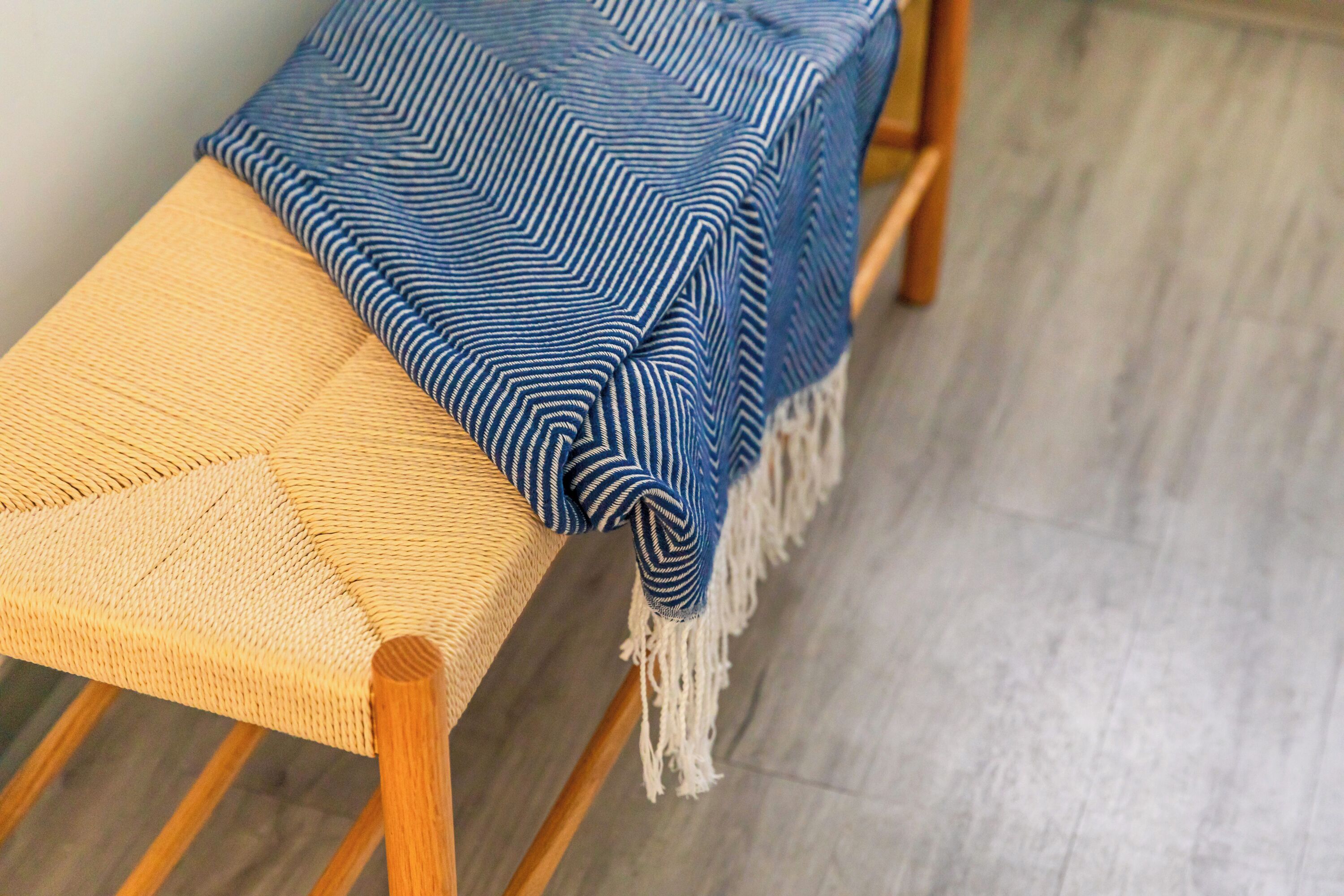 Een houten bank met een gevlochten zitting en een blauw-witte strepenkleurige deken eroverheen.