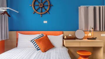 Una cama bien hecha con almohadas a rayas y lisas, una rueda de barco de madera en la pared, una mesita de noche con lámpara y un taburete naranja moderno.