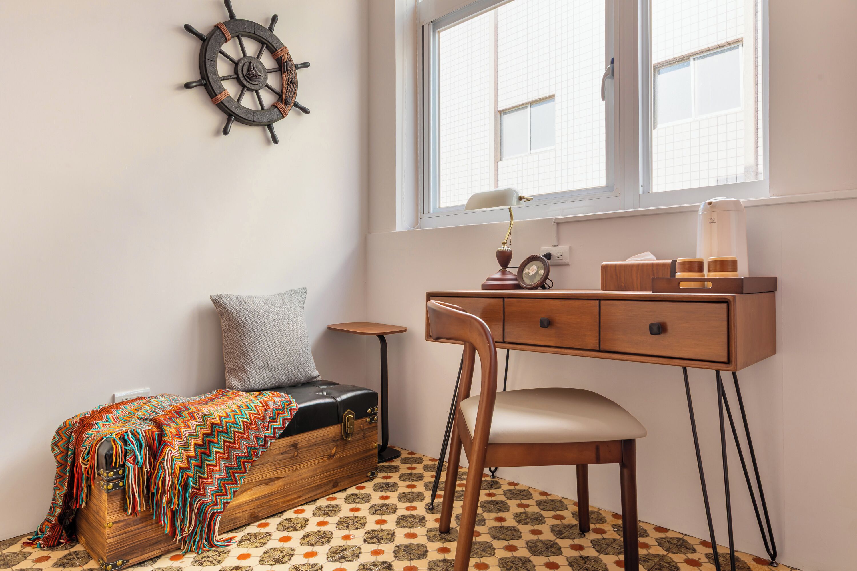Una habitación compacta con cama, escritorio, silla, mesita, un reloj de pared y ventana con vistas a edificios.