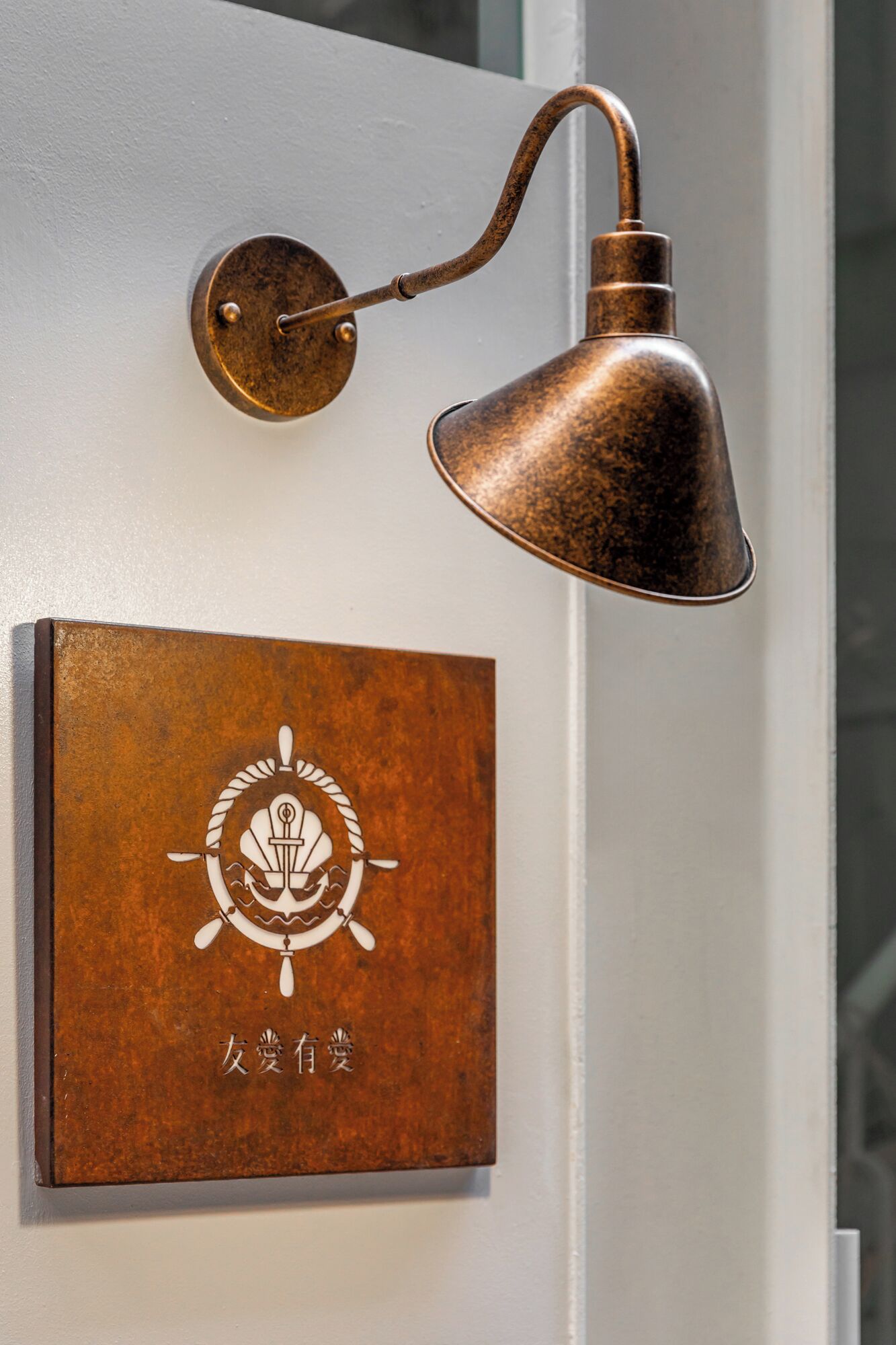 Luminária de bronze fixada na parede, com braço curvo e porta branca com uma placa de bronze com um símbolo e caracteres chineses.