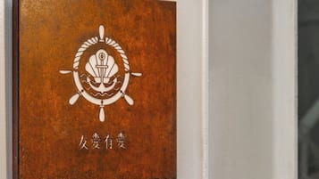 Luminária de bronze fixada na parede, com braço curvo e porta branca com uma placa de bronze com um símbolo e caracteres chineses.