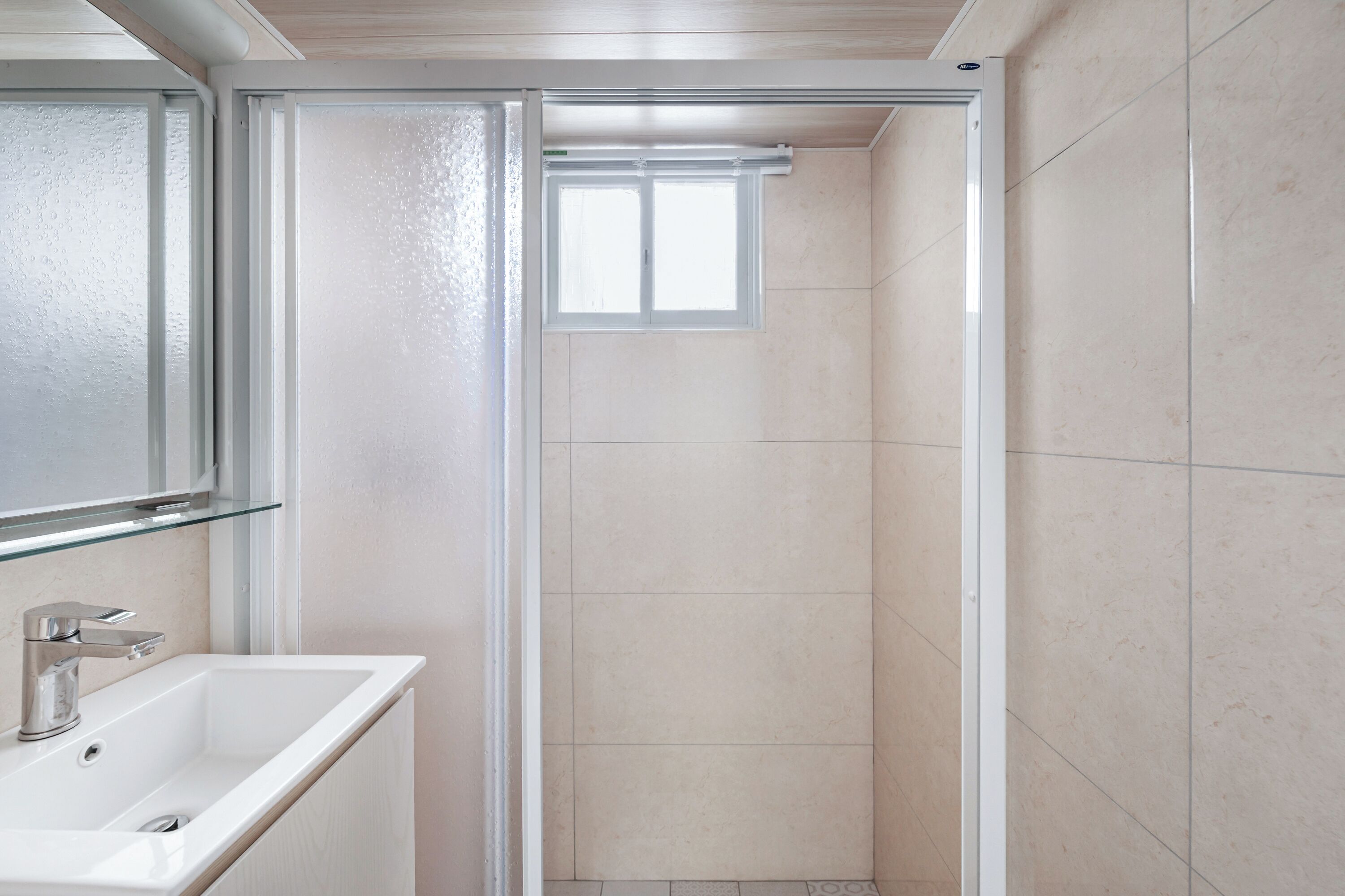 Un baño con lavamanos blanco, un espejo y una ducha con ventana.