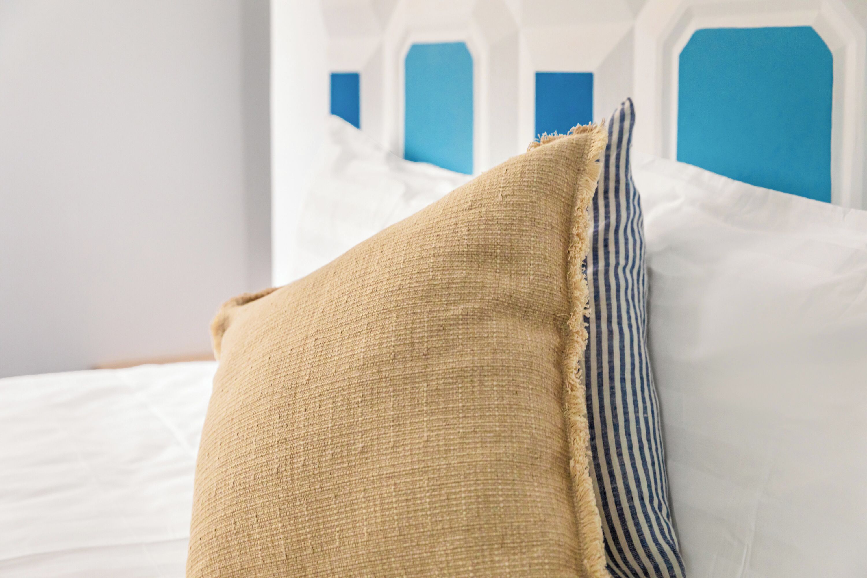 A bed with white bedding, a beige pillow, and a striped pillow.