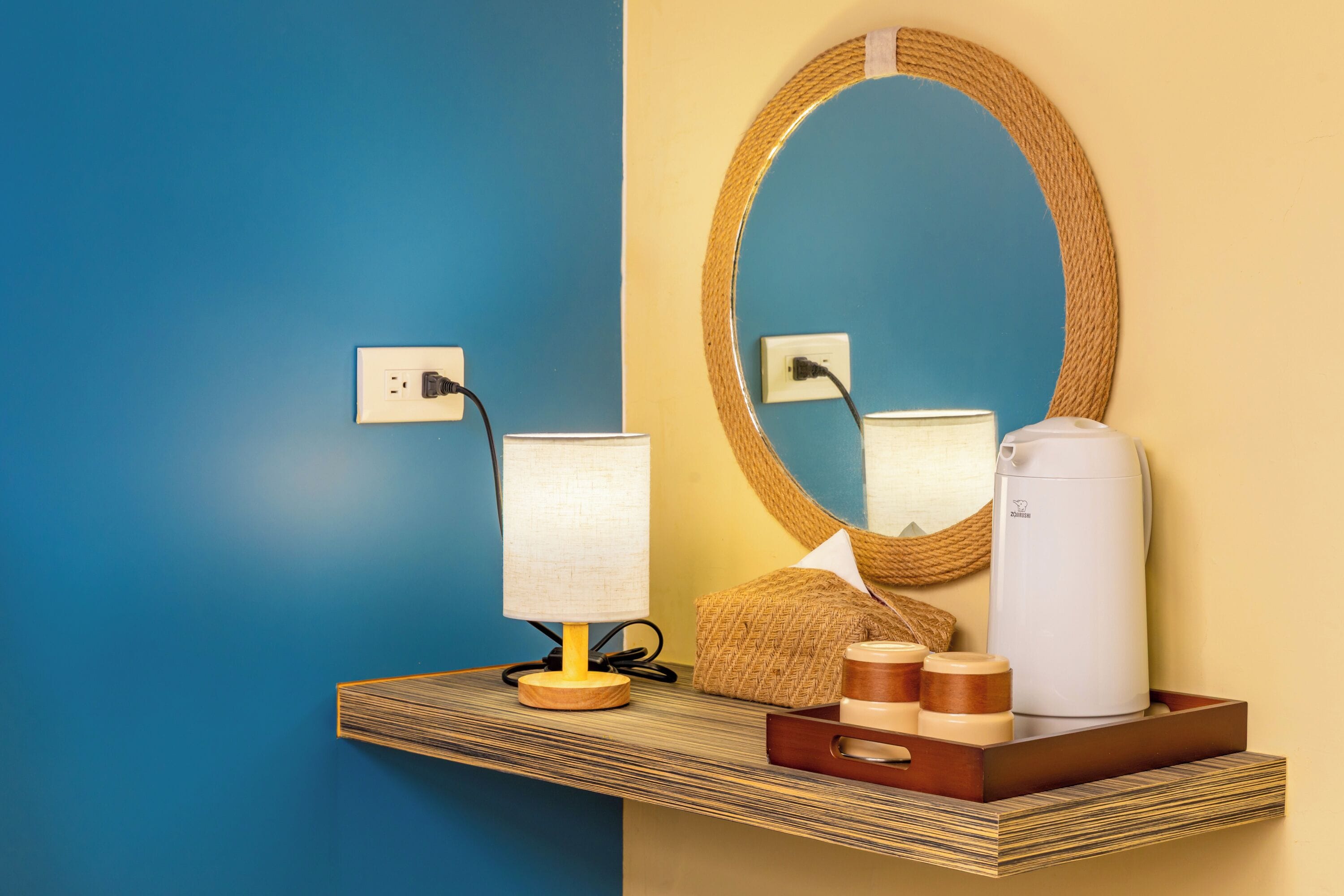 Una habitación con pared azul y amarilla, una estantería de madera con una lámpara, una cafetera y una cesta tejida.