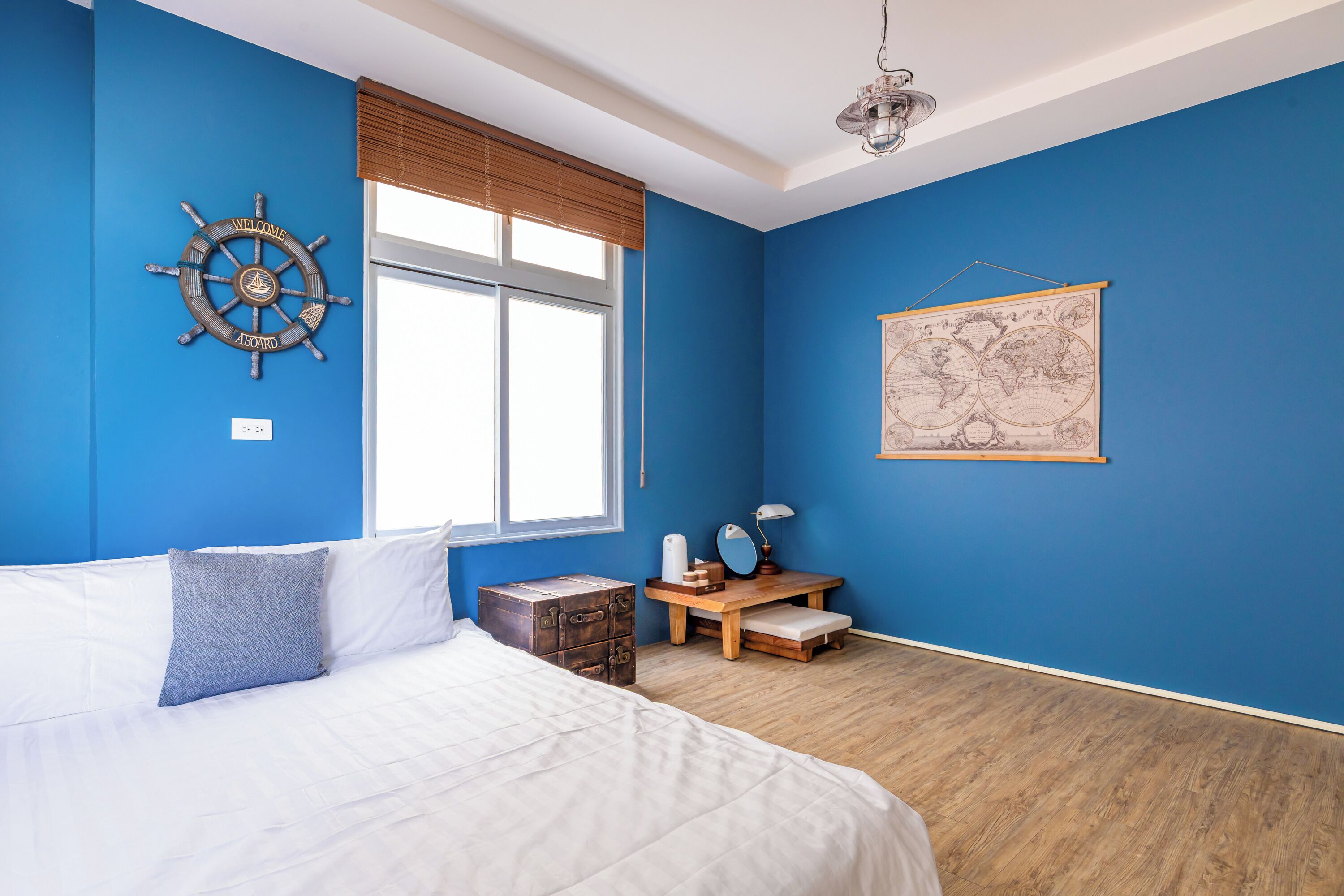 A bedroom with a large bed, a wooden chest, a desk with a mirror, and a world map on the wall.