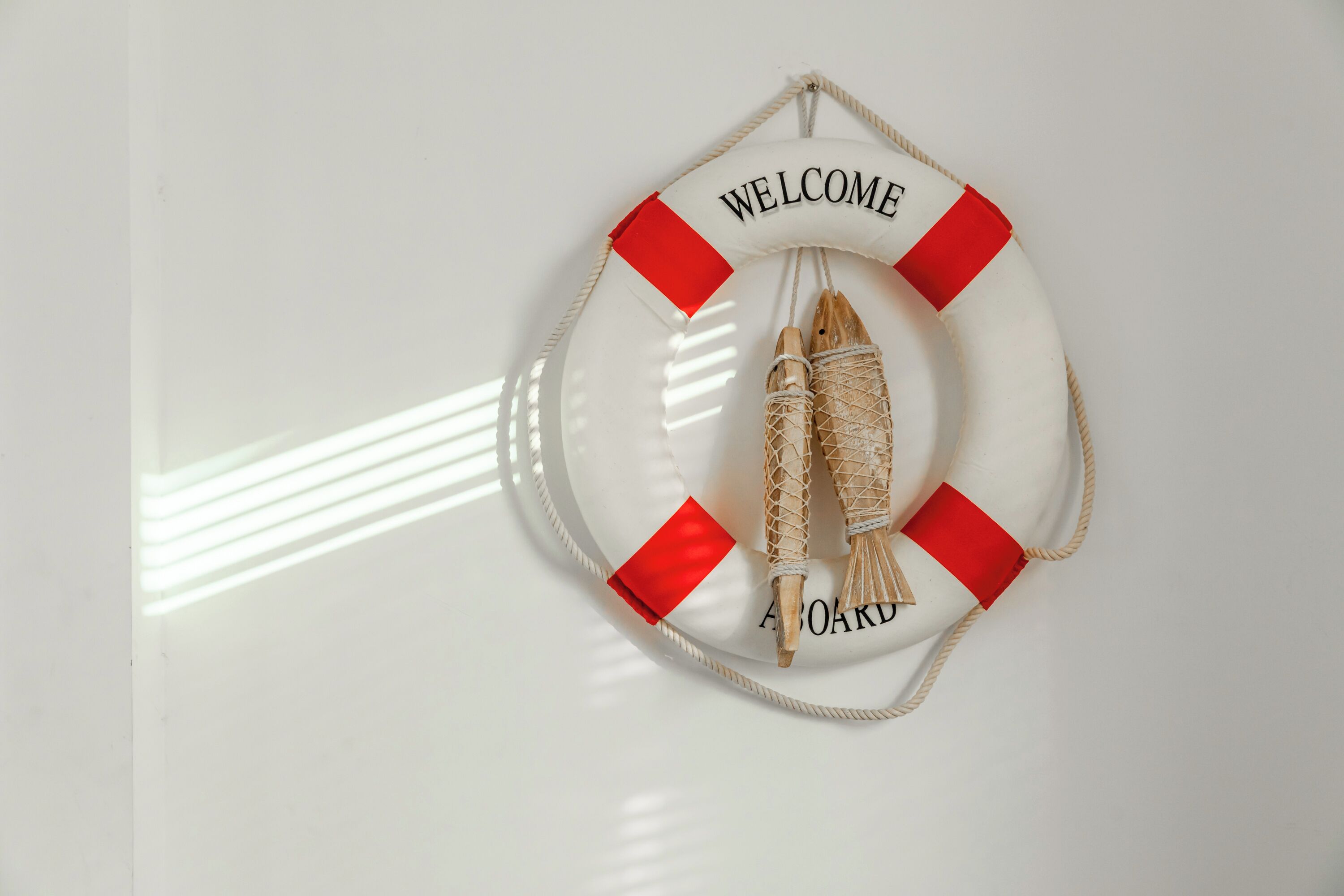 A life preserver with "WELCOME" and "BOARD" text, and two wooden fish tied to it.