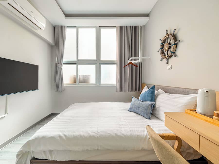 Una habitación de hotel moderna con una cama grande, un televisor de pantalla plana, un escritorio de madera y una decoración con timón de barco.