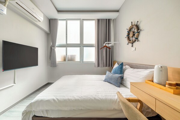 A modern hotel room with a large bed, a flat-screen TV, a wooden desk, and a ship's wheel decoration.