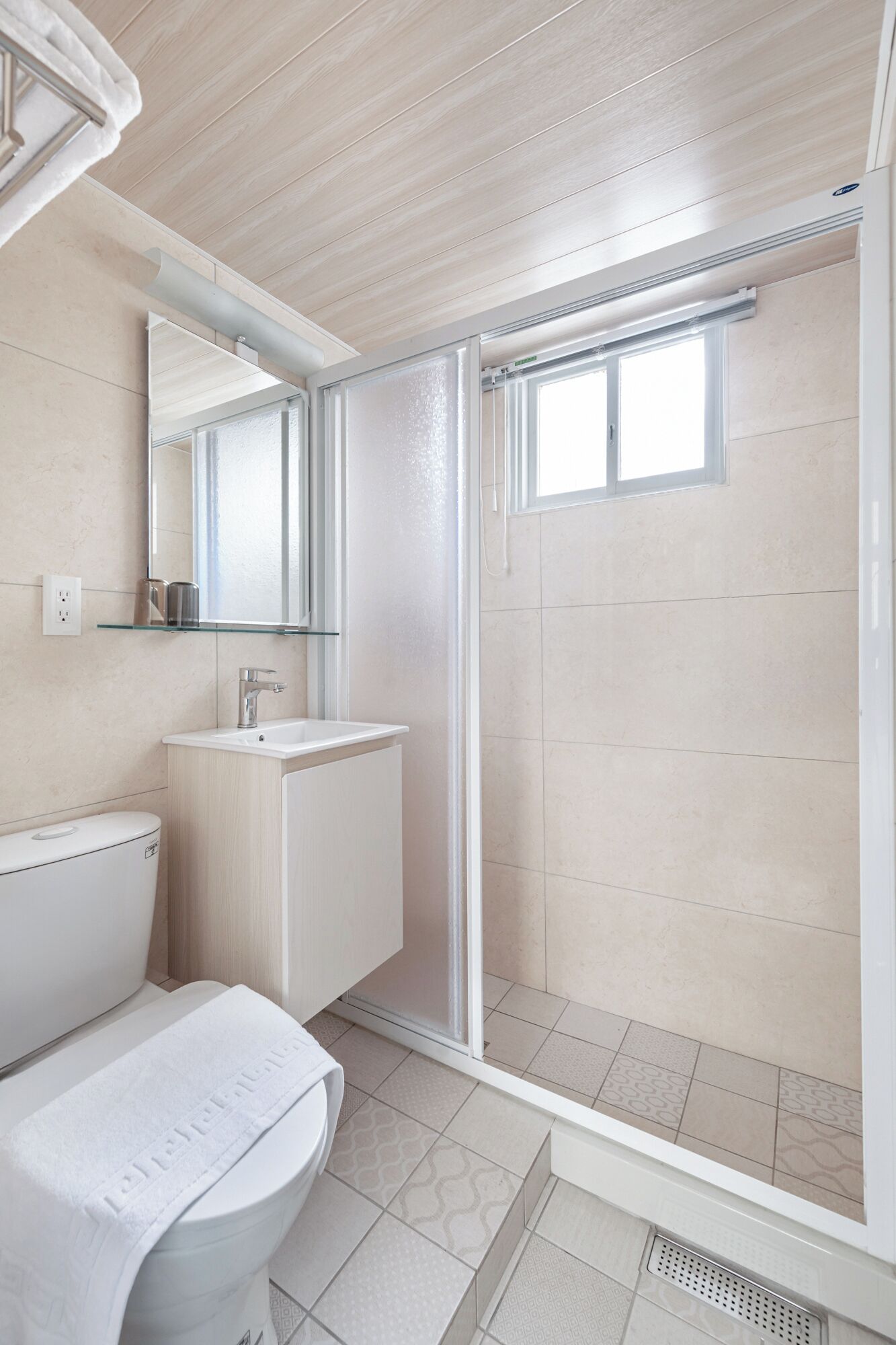 Un baño moderno con cabina de ducha de vidrio, un lavabo blanco y un inodoro.