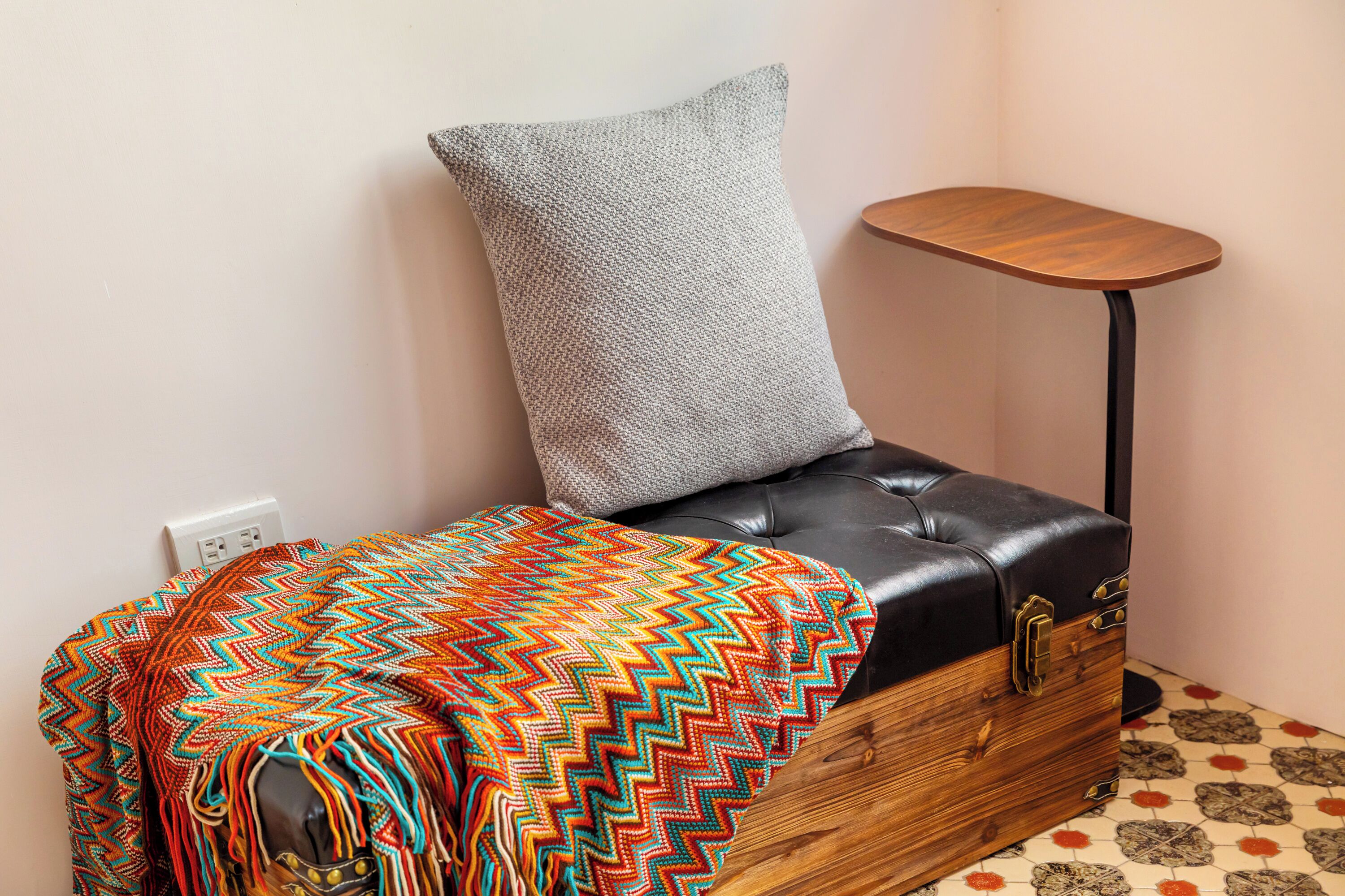 A corner room with a leather sofa, a patterned throw blanket, a small wooden side table, and a grey pillow.